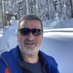 Christian, Dein Zuhörer steht im Schnee vor einem Wald und lächelt in die Kamera mit einer Sonnenbrille. Denn die Sonne scheint.