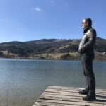 Christian, Dein Zuhörer steht auf einem Steg am See und blickt in die Landschaft - mit erhobenem Haupt, einem Lächeln und mit einem zufriedenen Gesamtausdruck (Gesicht, Körperhaltung).