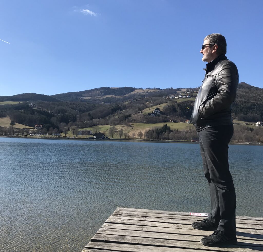 Mann steht ruhig auf einem Steg am See und blickt in die Weite – Symbol für Gelassenheit und innere Ruhe