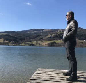 Mann steht ruhig auf einem Steg am See und blickt in die Weite – Symbol für Gelassenheit und innere Ruhe