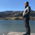 Mann steht ruhig auf einem Steg am See und blickt in die Weite – Symbol für Gelassenheit und innere Ruhe